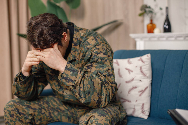 Portrait of young sad, desperate military man sitting on a coach during therapy session. Soldier lower head and hide his face. Man wearing camouflage. - Foto, immagini