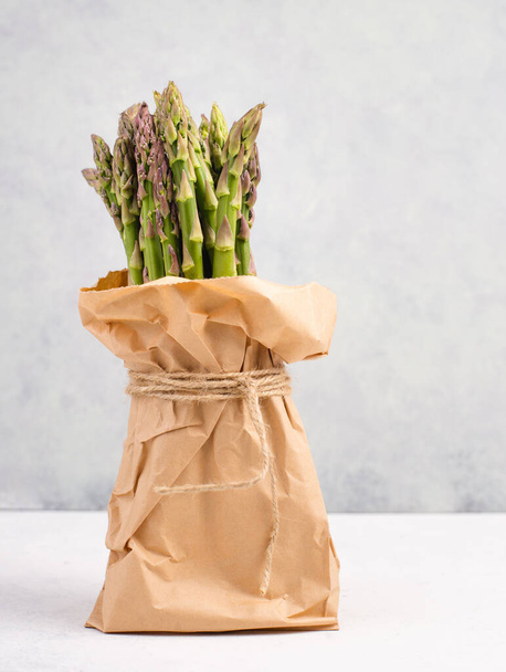 Fresh green bundle of asparagus on a white textured table, vegetables in spring, gourmet cuisine food, cooking a vegan meal - Zdjęcie, obraz