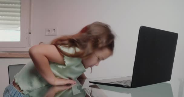 Küçük kız, internetten ders almak için cam masada dizüstü bilgisayarını açıyor. Uzun saçlı tatlı kız evde modern aletler kullanıyor. - Video, Çekim