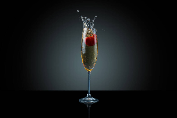 captured movement. Champagne splashes and falling strawberries on dark background. - Foto, afbeelding