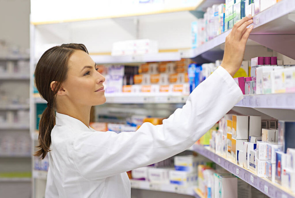 Shot of an attractive young pharmacist checking stock in an aisle. - Photo, Image