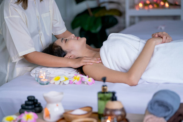Mooie Aziatische vrouw gevoel ontspannen en verlichten tijdens liggen op bed en krijgen spa massage met verschillende accessoires in de voorkant van bed. - Foto, afbeelding