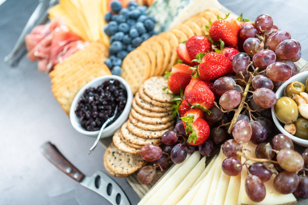 Fromage gastronomique, craquelins et fruits servis en entrée sur une planche à découper en bois. - Photo, image