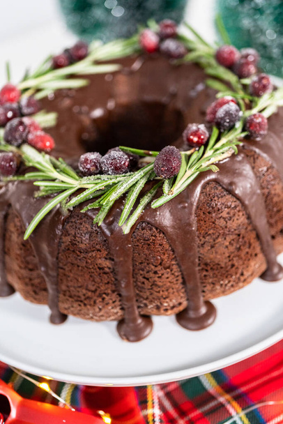 Čokoládový koláč s čokoládovou polevou zdobený čerstvými brusinkami a rozmarýnem pokrytý bílým cukrem. - Fotografie, Obrázek