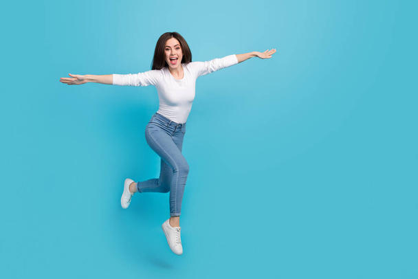 Photo of funky sweet lady dressed white shirt arms sides flying jumping high isolated blue color background. - Fotó, kép