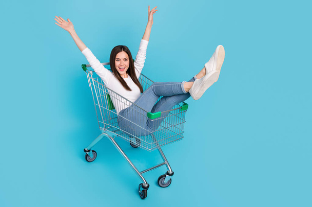 Photo of cute excited woman wear white shirt riding shopping tray rising arms isolated blue color background. - Foto, Bild