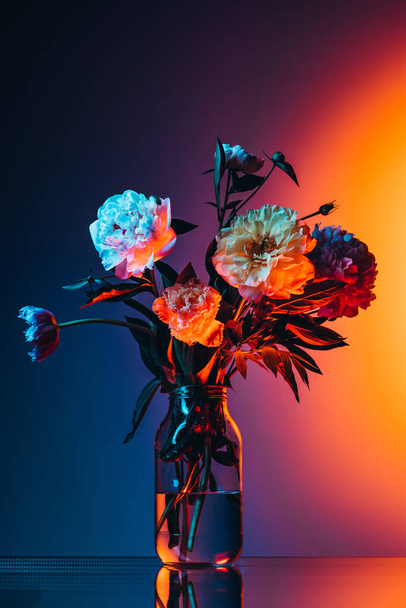 Flowers for beloved woman. Creative floral composition, gerberas, roses and peonies over dark background in neon light. Concept of floristry, decorations, garden, decor and ad. Design for wallpaper - 写真・画像
