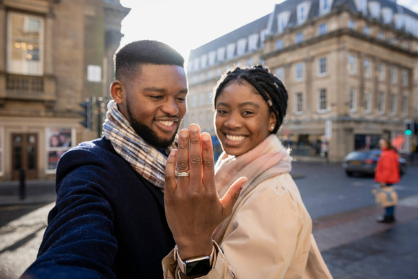 Cheerful couple in town, woman holging hand up to show engagement ring - Foto, Imagem