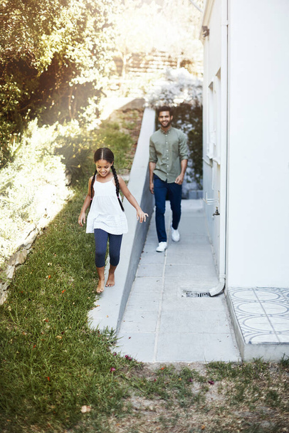Foto de una joven feliz yendo a dar un paseo por el patio trasero con su padre detrás de ella. - Foto, Imagen