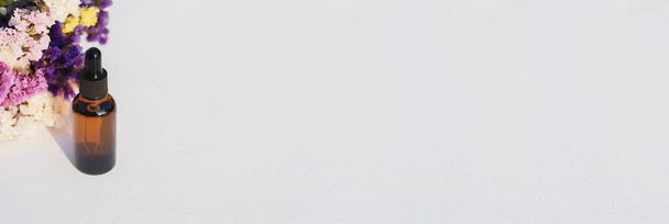 Μπουκάλι γυάλινο πορτοκαλί σταγονόμετρο σε λευκό φόντο με ξηρά λουλούδια. Περιέκτης mockup με καλλυντικό έλαιο ή ορό. Προθήκη για τα προϊόντα περιποίησης δέρματος παρουσίασης. - Φωτογραφία, εικόνα