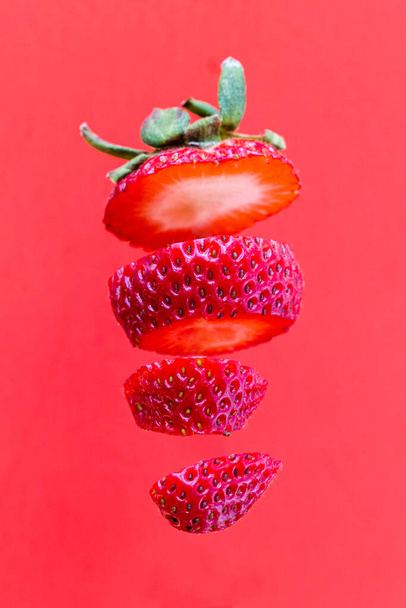 Close up of a sliced strawberry floating over a red background - Foto, Imagem