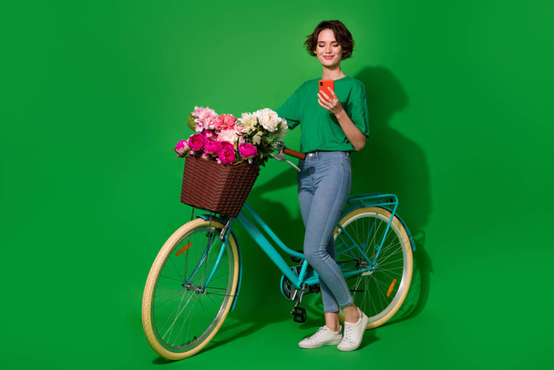Full body portrait of gorgeous nice lady standing near bike use telephone isolated on green color background. - Photo, image