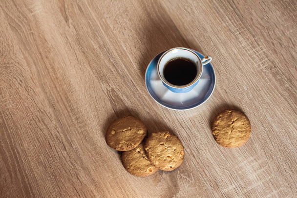 Ένα φλιτζάνι ζεστό αρωματικό μαύρο καφέ σε ένα πιατάκι με μπισκότα, σε ένα ξύλινο ανοιχτό καφέ υφή τραπέζι. - Φωτογραφία, εικόνα