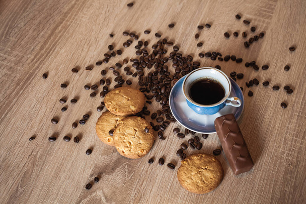 Kawa palona ziarna i filiżanka kawy z napojem na ciemnej drewnianej powierzchni, w pobliżu leży czekolada i apetyczne ciasteczka. - Zdjęcie, obraz