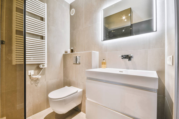 Modern flush toilet and ceramic sink installed on white tiled walls near mirror and towel in small restroom at home - Fotoğraf, Görsel
