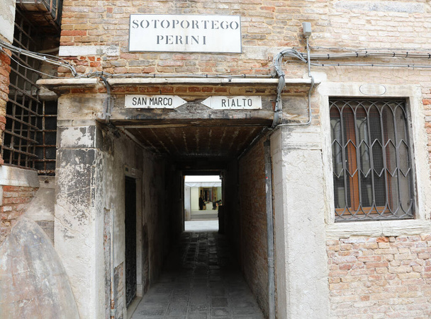 Calle estrecha de Venecia en Italia y el texto que significa Bajo el Porche llamado PERINI y la indicación a la Plaza de San Marcos o Puente de Rialto en lengua italiana - Foto, Imagen