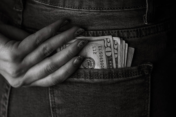La adolescente toma billetes de dólar de su bolsillo trasero. Los billetes se cierran, el dinero en el bolsillo de un vaquero. Dólares sobresalen del bolsillo de los vaqueros, concepto de moneda de dinero
 - Foto, imagen