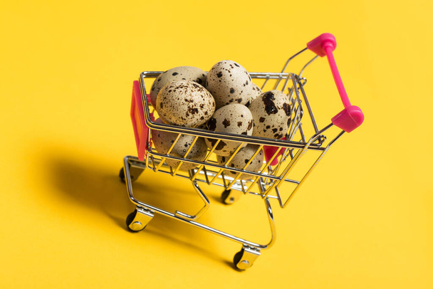 Small quail eggs in a shopping cart on a yellow background, healthy food - Photo, Image