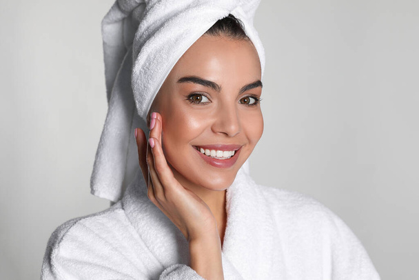 Beautiful young woman wearing bathrobe and towel on head against light background - Valokuva, kuva