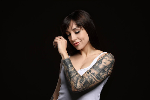 Beautiful woman with tattoos on arm against black background - Fotoğraf, Görsel