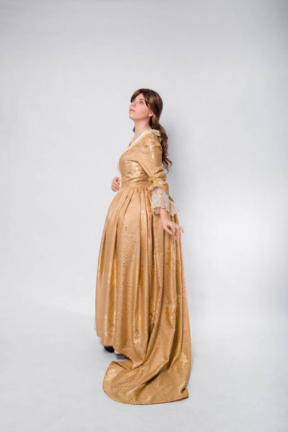 Full length portrait of a woman in a gold dress in the style of the rococo era, standing with her back forward and posing isolated on a white background. - Foto, afbeelding