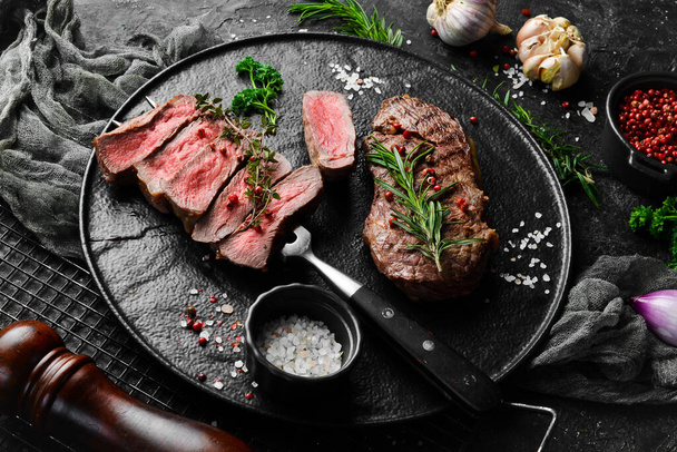 Grilled ribeye beef steak. Steak on a fork on a black plate. Top view. On a black stone background. - Foto, Imagem