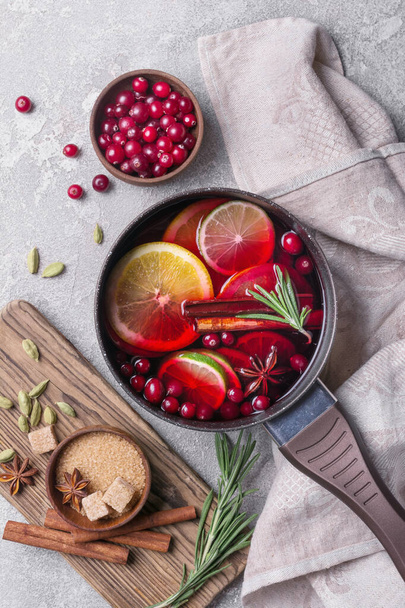 Autumn or christmas traditional drink with apples, oranges, cranberry, cinnamon, rosemary and other ingredients on grey concrete background - Фото, изображение