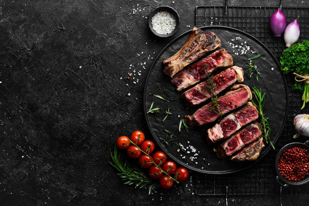 Veal steak on a bone. Juicy pieces of steak. Free space for your text. Top view. On a black stone background. - 写真・画像
