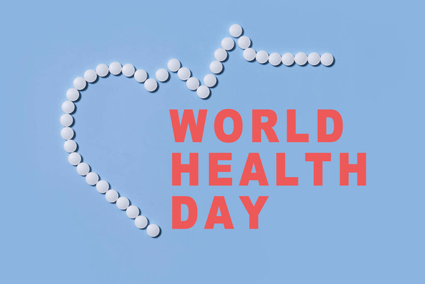 Gruppe weißer, runder Pillen formt Herzfigur neben Herzrhythmus aus weißen Pillen auf blauem Hintergrund. Thema Gesundheitsfürsorge, medizinische Behandlung und Krankheitsprävention. - Foto, Bild