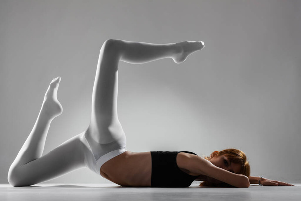 Fit ballerina girl lying and stretching practicing yoga poses against gray background. - Foto, Imagen
