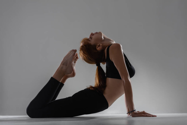 Fit ballerina girl lying and stretching practicing yoga poses against gray background. - 写真・画像