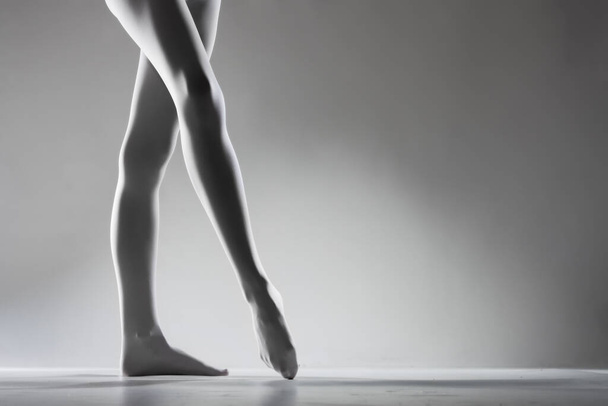Sexy female legs with white leggings standing ballerina pose on gray background. - Foto, Bild