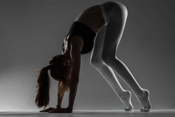 Fit ballerina girl stretching and practicing yoga poses against gray background. - Foto, Bild