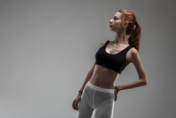 Fit girl with black top and white leggings posing against gray background. - Zdjęcie, obraz