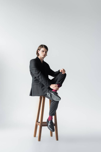 Full length of stylish man sitting on chair on grey background - Foto, immagini