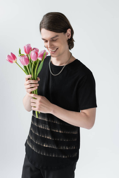 Happy stylish man holding tulips isolated on grey  - Фото, изображение