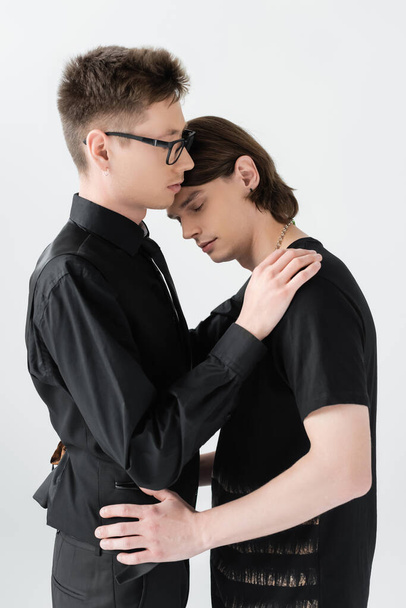Young gay in eyeglasses hugging brunette boyfriend isolated on grey  - Photo, Image