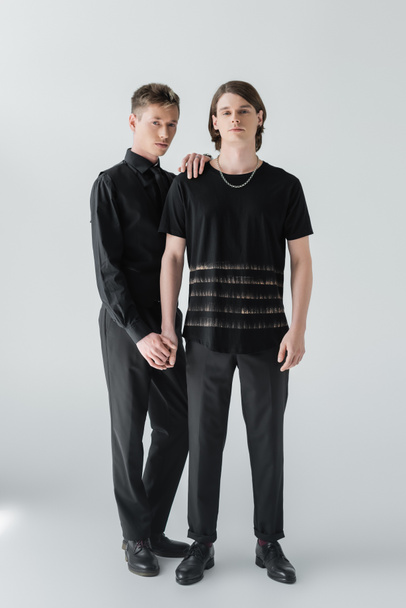 Full length of stylish gay couple holding hands on grey background  - 写真・画像