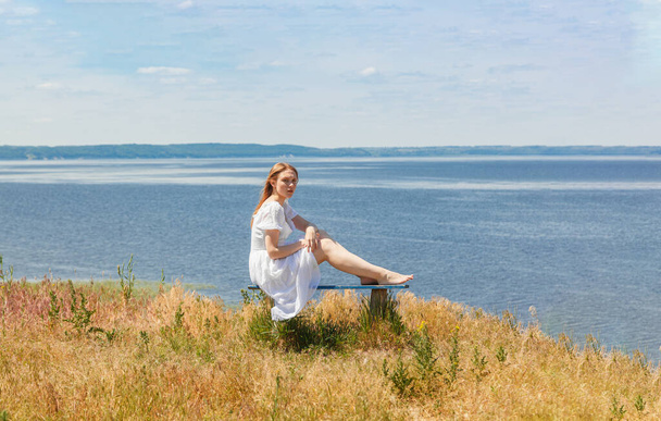 Krásná dívka sedí na lavičkách na pobřeží s výhledem na oblohu zblízka - Fotografie, Obrázek