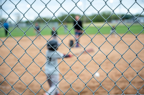 Selective focus on chain link fence with a youth baseball game defocused and blurred in the background. High quality photo - Fotografie, Obrázek