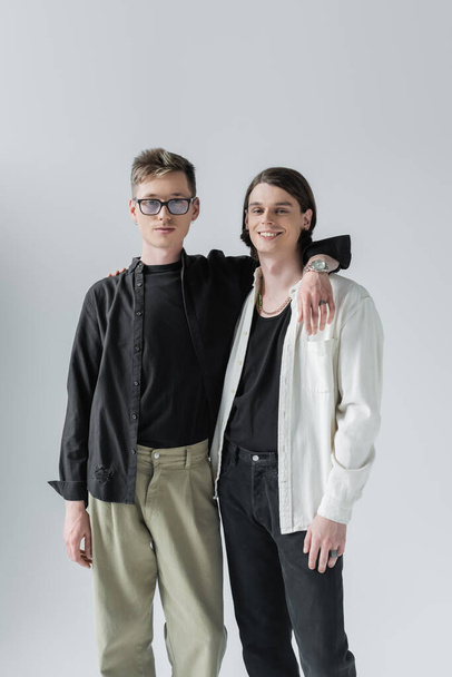 Stylish same sex couple looking at camera while hugging isolated on grey  - Foto, immagini