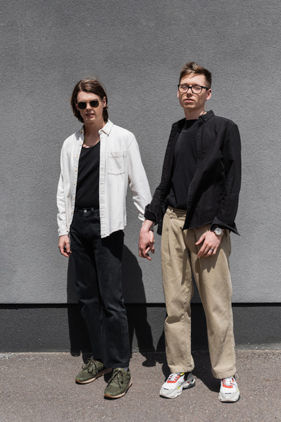 Trendy homosexual couple holding hands near building outdoors  - Фото, изображение