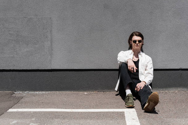 Stylish man in sunglasses sitting near building on urban street  - Valokuva, kuva