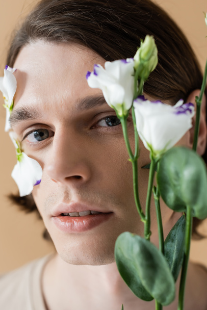 Portrait of young man looking at camera near blurred eustoma flower isolated on beige  - Photo, Image