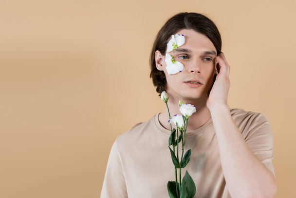 Portrait of young man holding eustoma and touching face isolated on beige  - Foto, Imagem