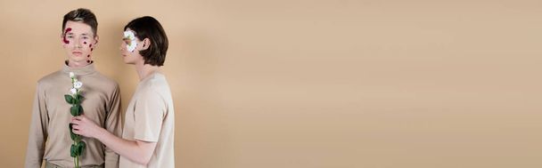 Morena hombre con pétalos sosteniendo eustoma cerca de novio aislado en beige, pancarta  - Foto, imagen