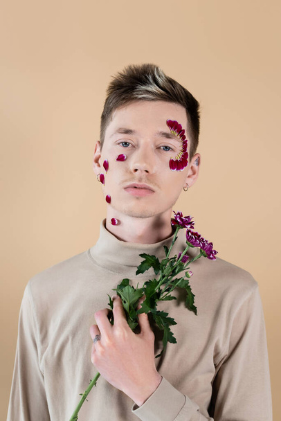 Young man wit petals on face holding chrysanthemums isolated on beige  - Foto, immagini