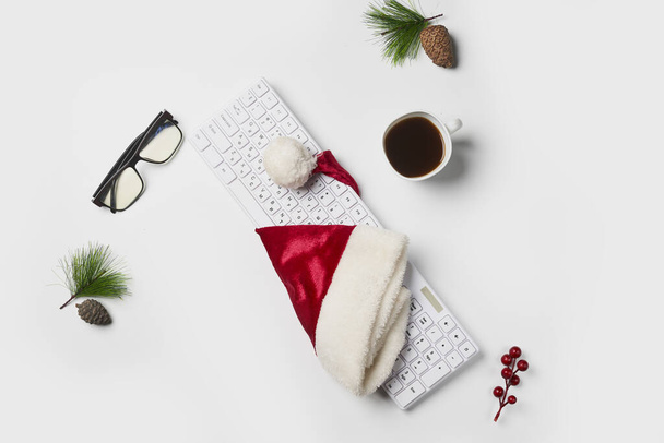 Karácsonyi vagy újévi háttér. Irodai asztal, mikulás kalap, karácsonyi dekoráció, billentyűzet, csésze kávé, szemüveg fehér háton. Lapos fekvés, felülnézet, másolás - Fotó, kép