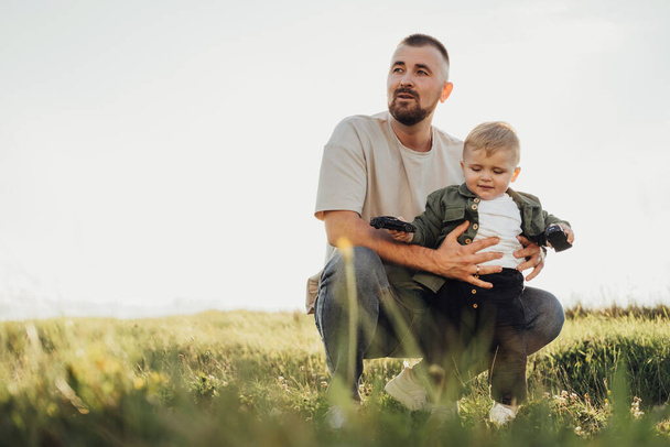 Ojciec trzymający swojego synka na polu, Portret taty i malucha na świeżym powietrzu - Zdjęcie, obraz