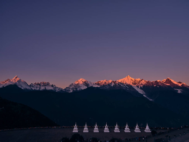 white pagodas of feilai temple with meili snow mountain at sunrise in background in china's yunnan province - Photo, Image
